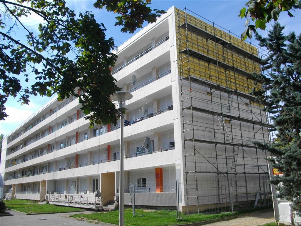 Cette image montre un immeuble résidentiel en pleine éco-réhabilitation, illustrant l'engagement envers des pratiques de construction durables. Les échafaudages entourant le bâtiment témoignent des travaux en cours pour améliorer l'isolation et l'efficacité énergétique, contribuant à un meilleur confort pour les résidents et à la réduction de l'empreinte écologique.